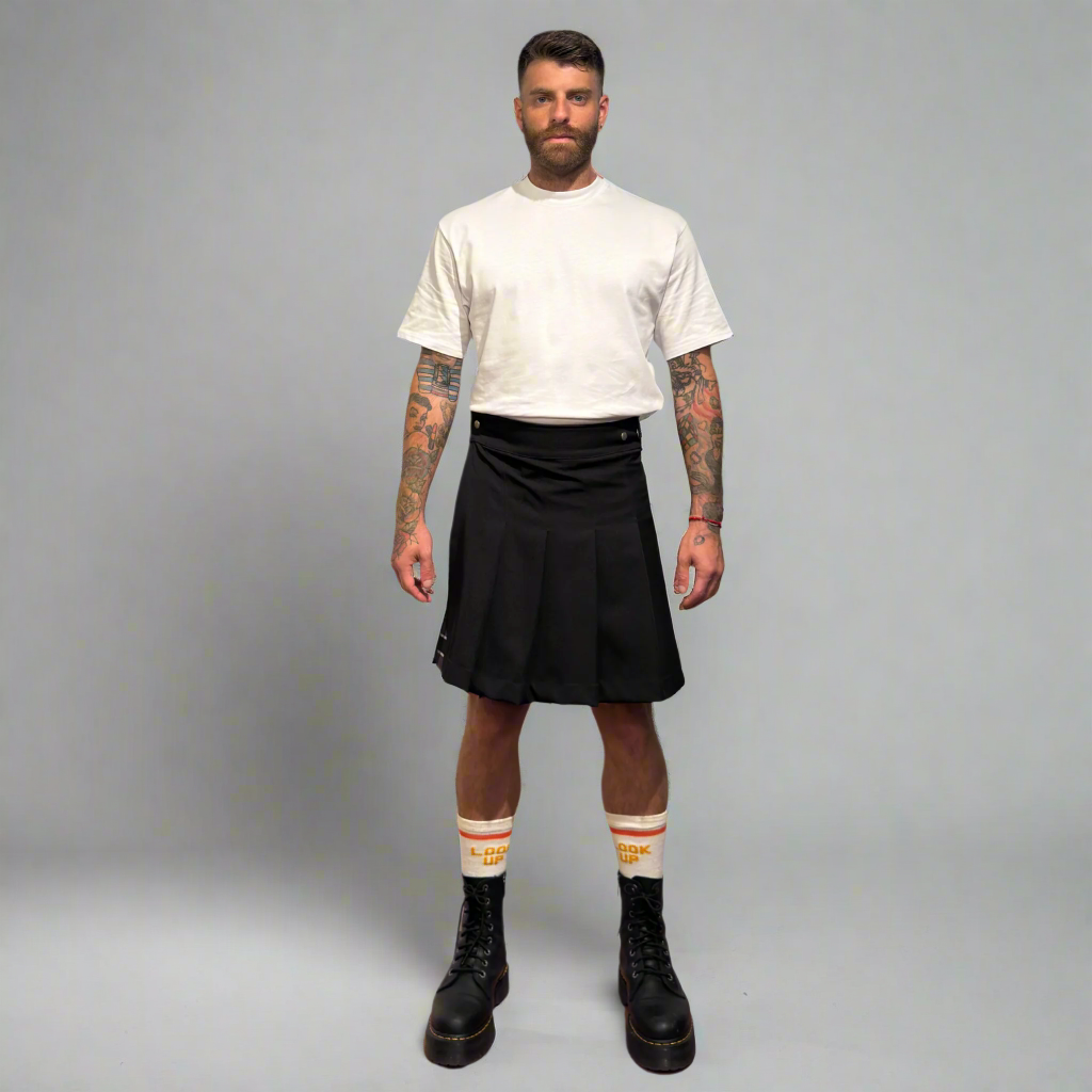 Man wearing a white t-shirt, black kilt, and black boots on a gray background