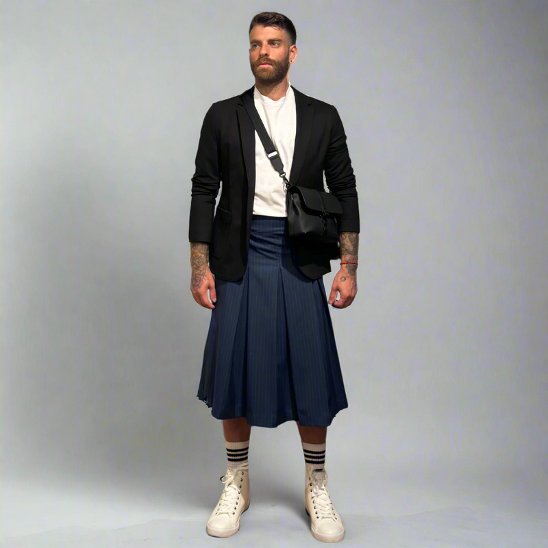 Man wearing a black blazer, white shirt, navy pleated kilt, and white sneakers on a gray background