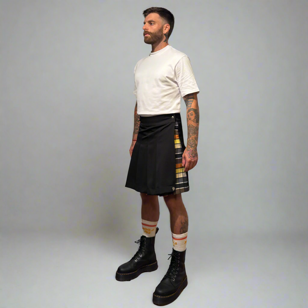 Man wearing a black kilt with a plaid pattern, white t-shirt, and black boots on a gray background