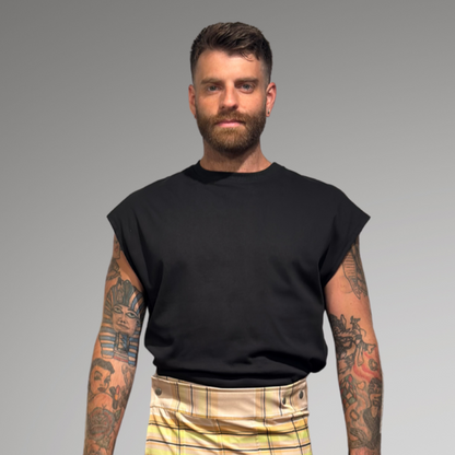 Man wearing a black sleeveless shirt and plaid  kilt against a gray background