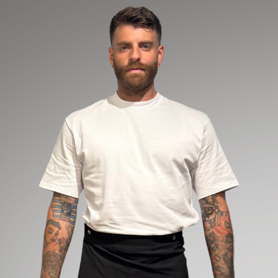Man wearing a white oversized t-shirt, black skirt, and black boots on a gray background