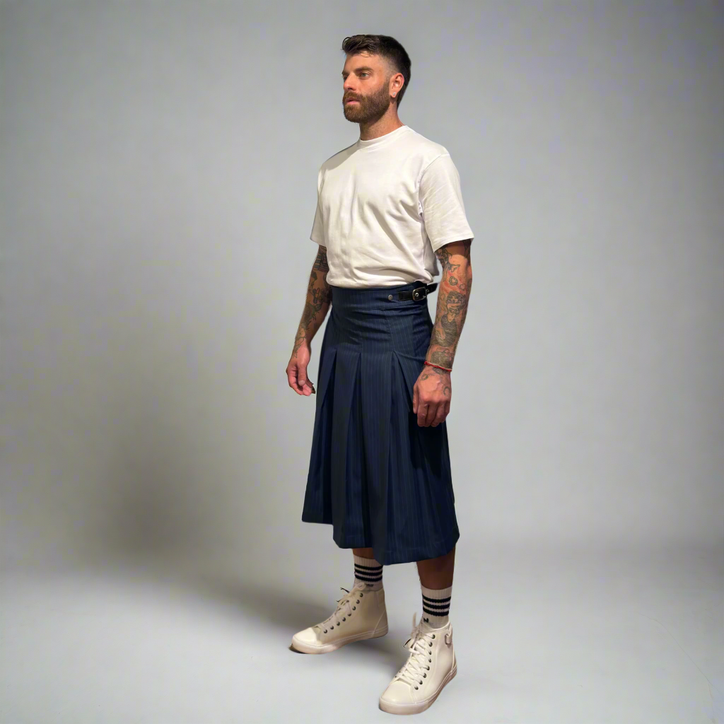 Man wearing a navy pleated kilt with a white t-shirt and white sneakers on a gray background