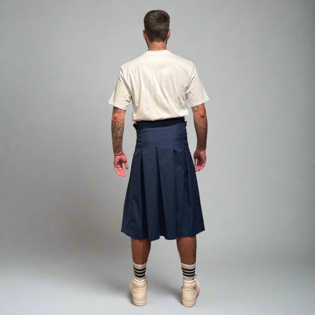 Man wearing a navy pleated kilt with a white t-shirt and white sneakers on a gray background