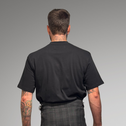 Man wearing a black oversized t-shirt and gray kilt on a gray background