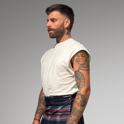 Man wearing a white sleeveless shirt and plaid kilt on a gray background