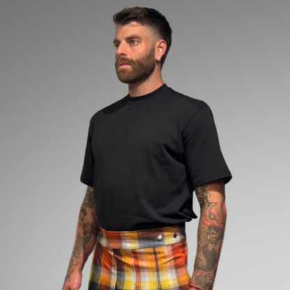 Man wearing a black oversized t-shirt plaid kilt on a gray background