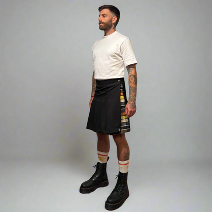 Man wearing a black kilt with a plaid pattern, white t-shirt, and black boots on a gray background