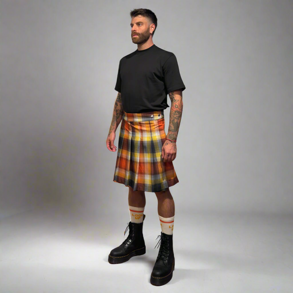 Man wearing a plaid kilt, black t-shirt, and black boots on a gray background