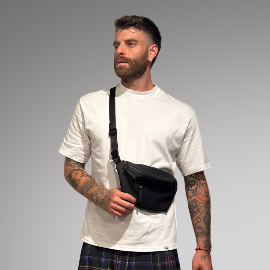 Man wearing a white t-shirt, plaid kilt, and white sneakers on a gray background