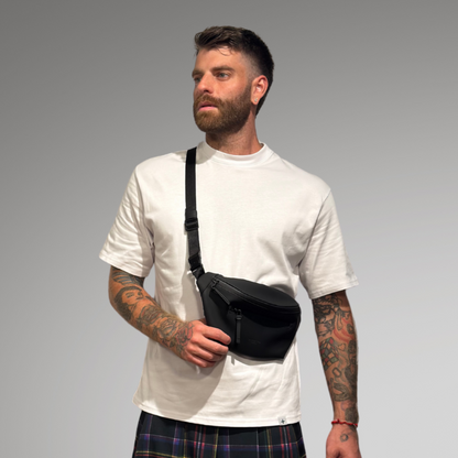 Man wearing a white t-shirt, plaid kilt, and white sneakers on a gray background