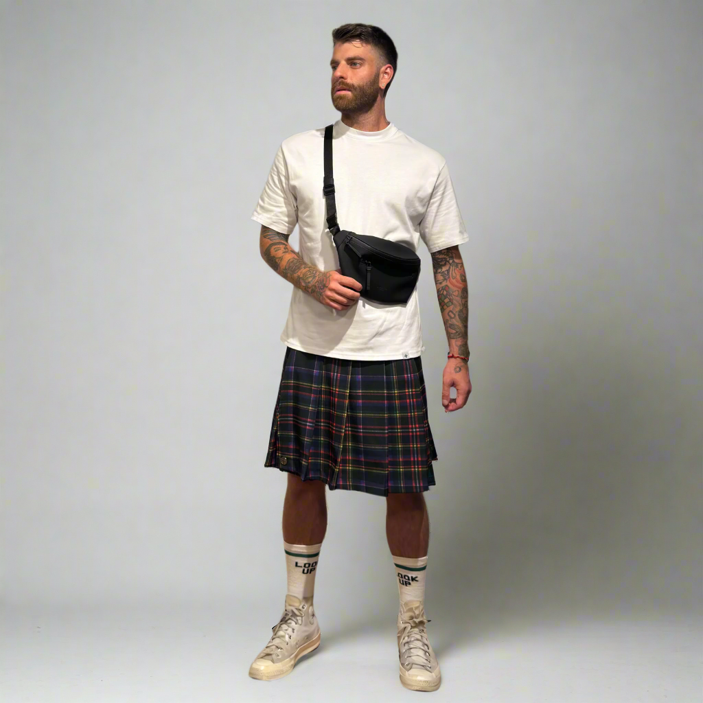 Man wearing a white t-shirt, plaid kilt, and beige sneakers on a plain background